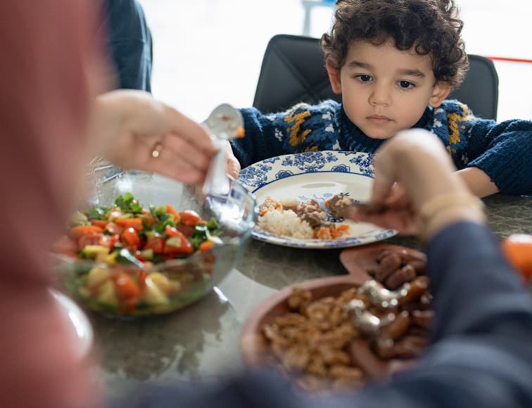Child waiting for food at the table while an adult serves a meal, highlighting hunger and the need for family food support.